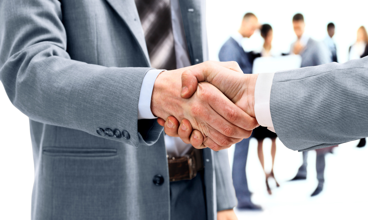 Two people in business attire shaking hands, with more people behind them out of focus